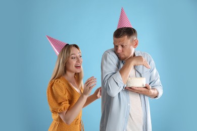 Greedy man hiding birthday cake from woman on turquoise background