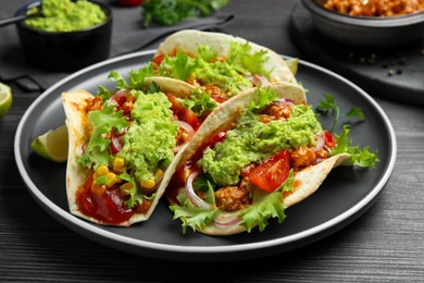 Delicious tacos with guacamole, meat and vegetables on wooden table, closeup