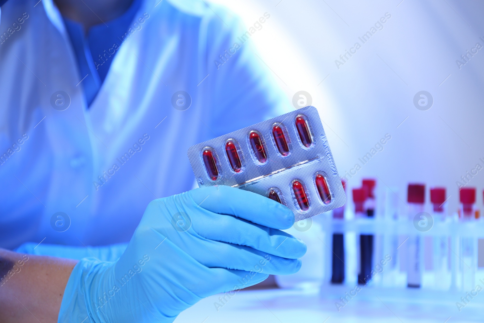 Photo of Scientist with pills at table in laboratory, closeup