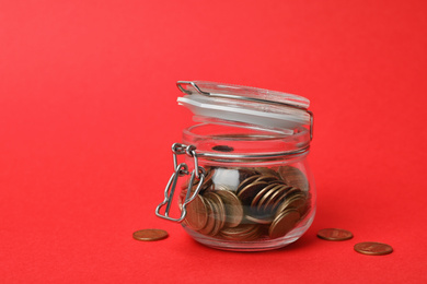 Glass jar with coins on red background