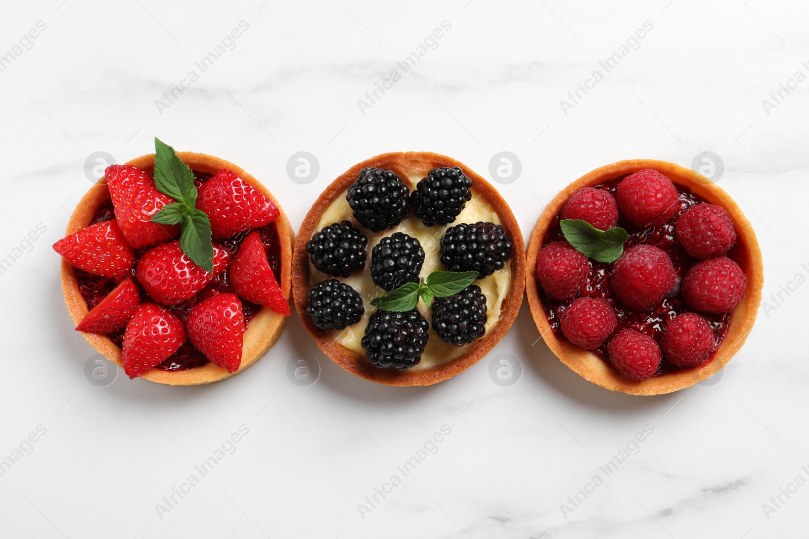 Photo of Tartlets with different fresh berries on white marble table, flat lay. Delicious dessert