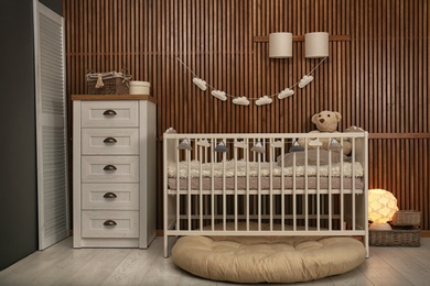 Photo of Baby room interior with crib near wooden wall