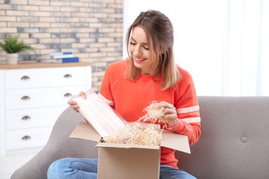 Young woman opening parcel on sofa in living room