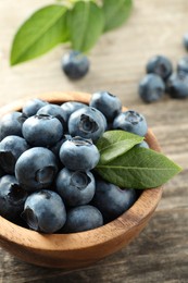 Photo of Bowl of tasty fresh blueberries on wooden table, closeup