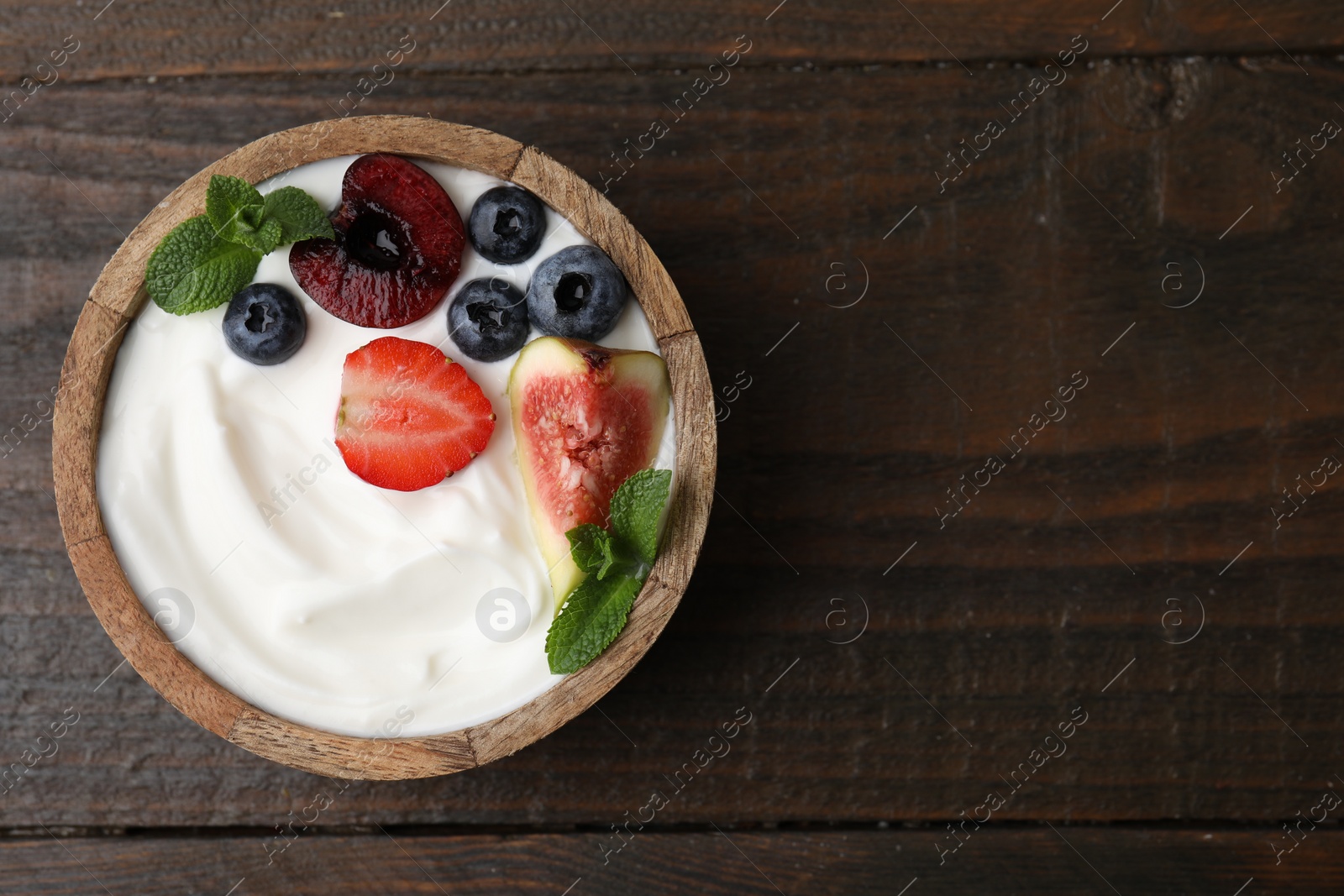 Photo of Bowl with yogurt, berries, fruits and mint on wooden table, top view. Space for text