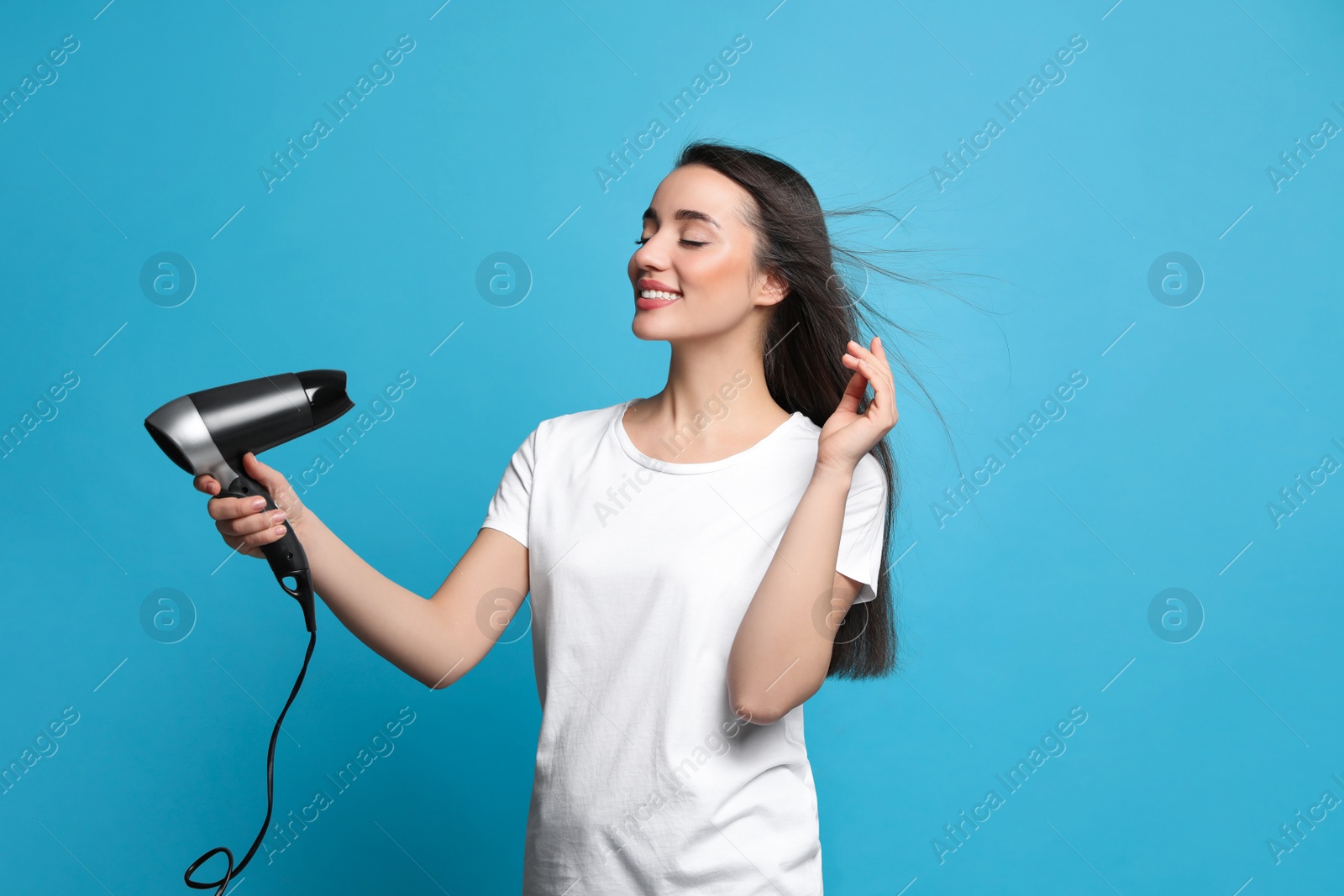 Photo of Beautiful young woman using hair dryer on light blue background