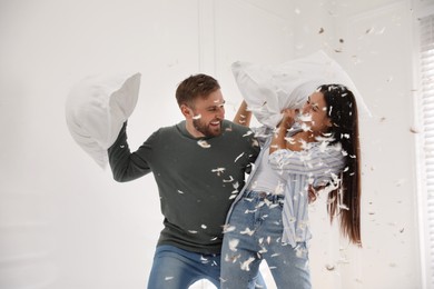 Happy young couple having fun pillow fight at home