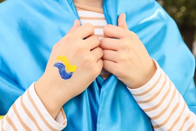 Photo of Woman with drawing of Ukrainian flag on hand against blurred background, closeup