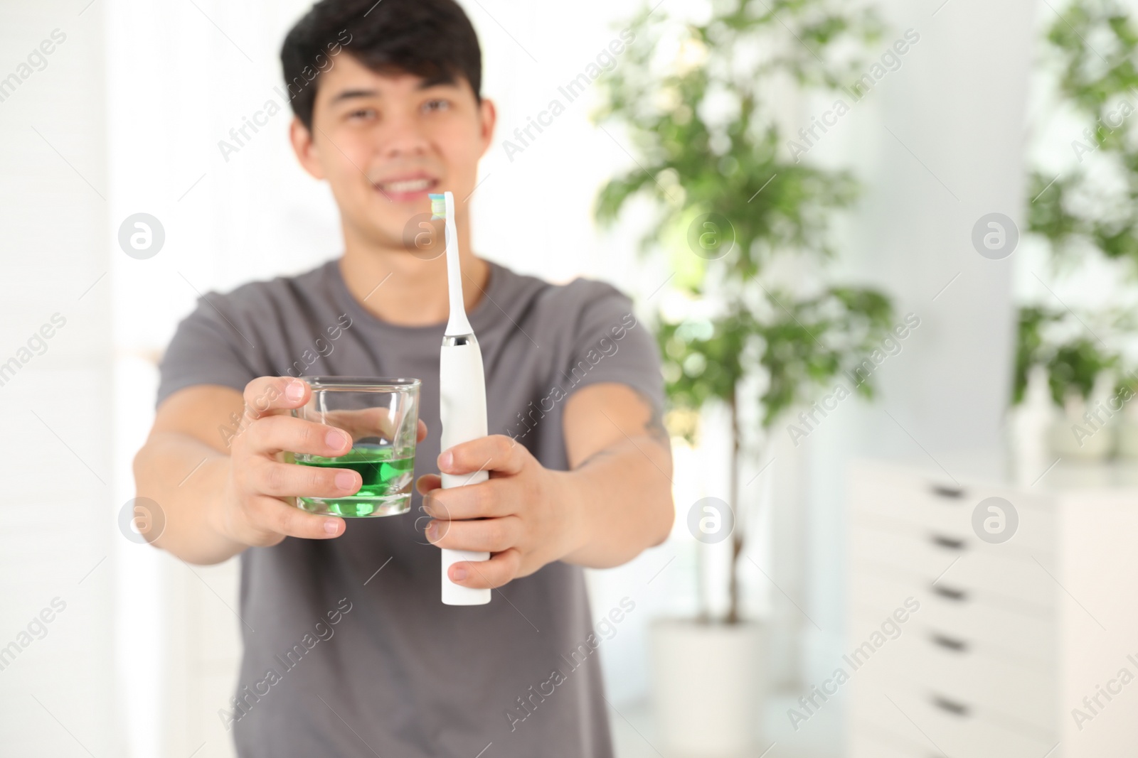 Photo of Man holding glass with mouthwash and toothbrush in bathroom, closeup. Teeth care