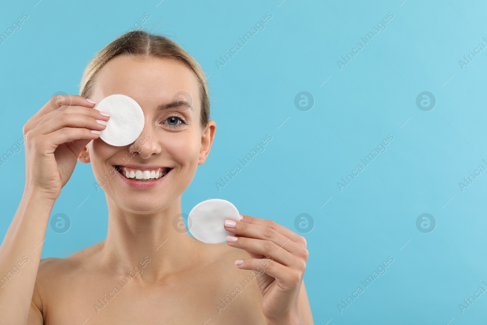 Photo of Smiling woman removing makeup with cotton pads on light blue background. Space for text