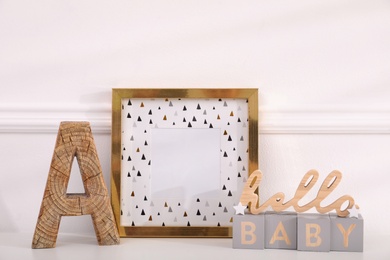 Photo of Empty photo frame, wooden letter A and decor near wall, space for text. Baby room interior element