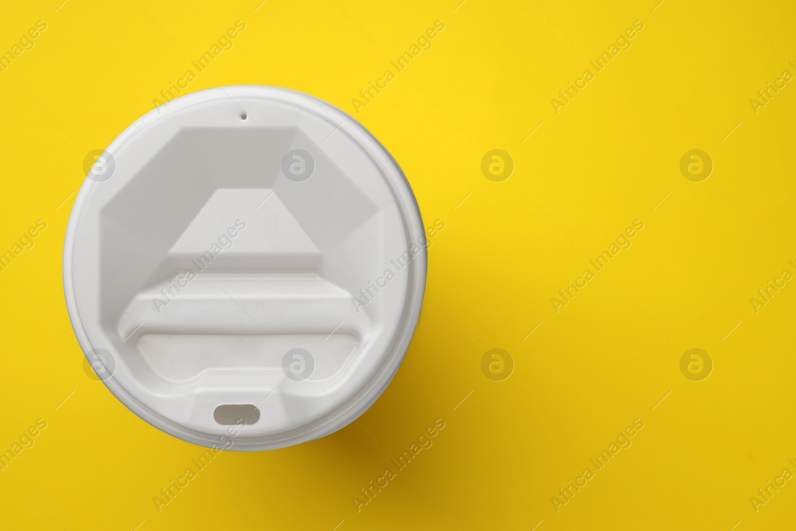 Photo of One paper cup with white lid on yellow background, top view with space for text. Coffee to go