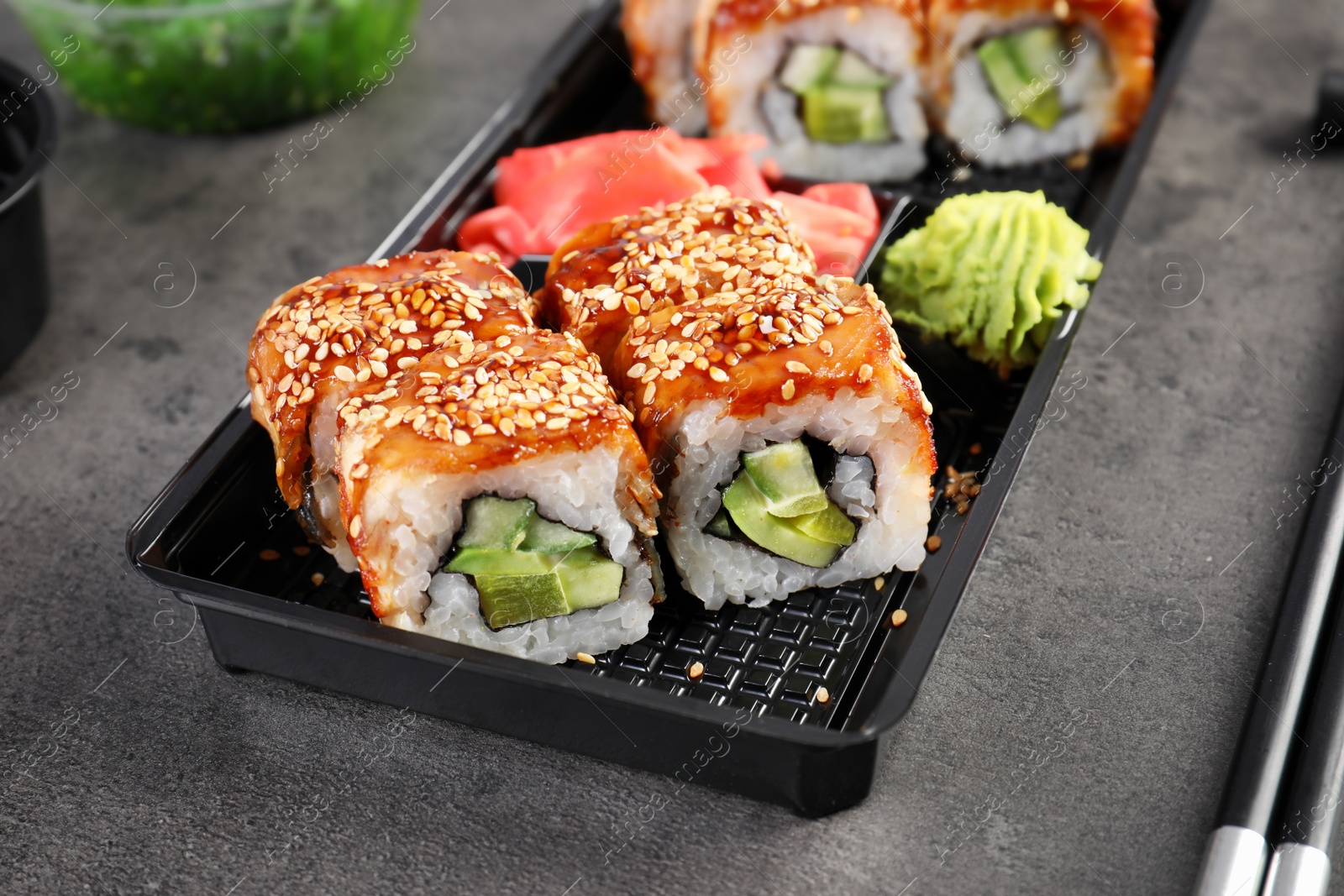 Photo of Box with tasty sushi rolls on grey table. Food delivery