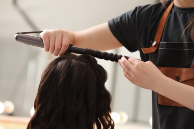 Photo of Hair styling. Hairdresser curling woman's hair in salon, closeup