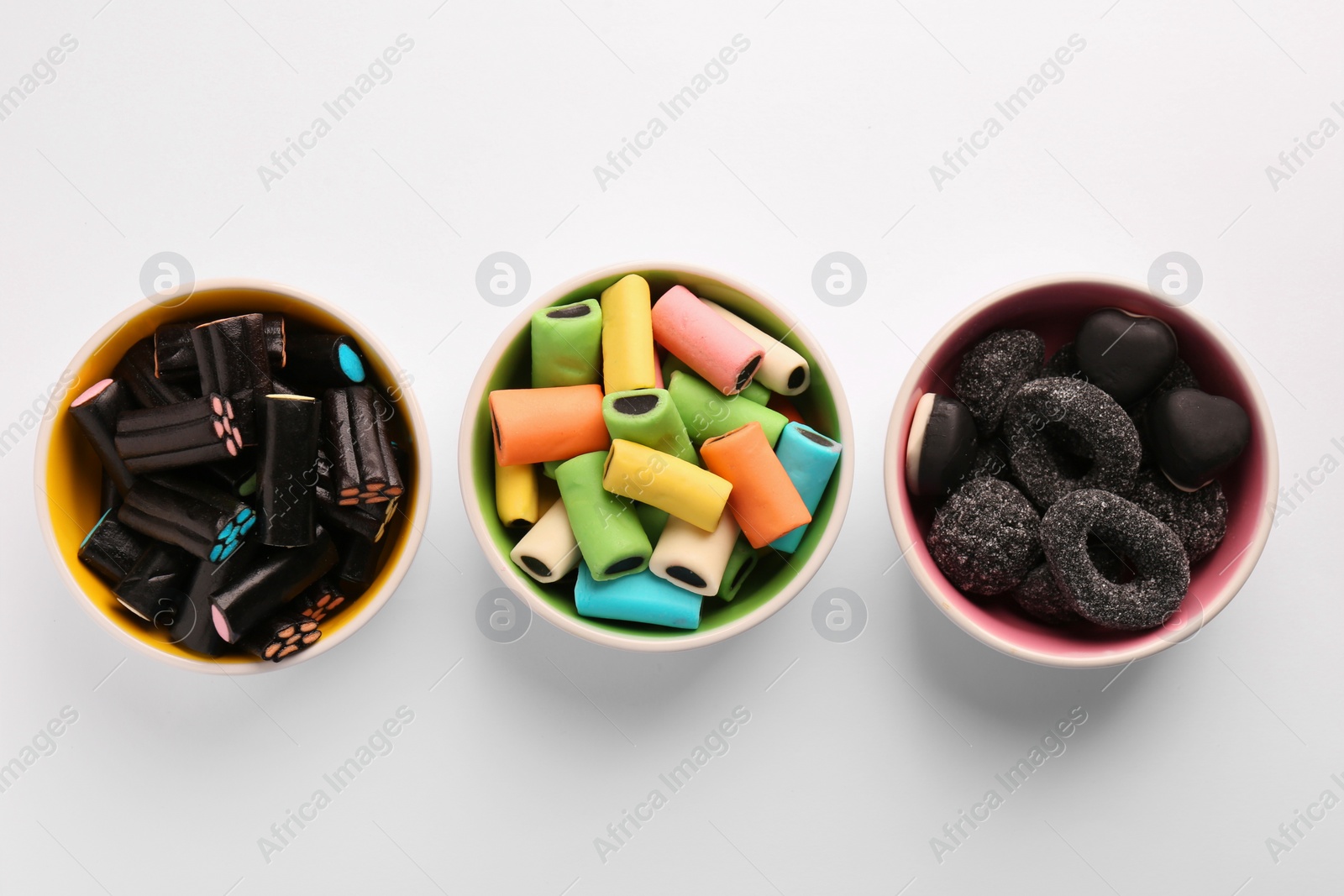 Photo of Bowls of tasty liquorice candies on light background, flat lay