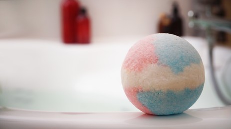 Colorful bath bomb on tub indoors, space for text