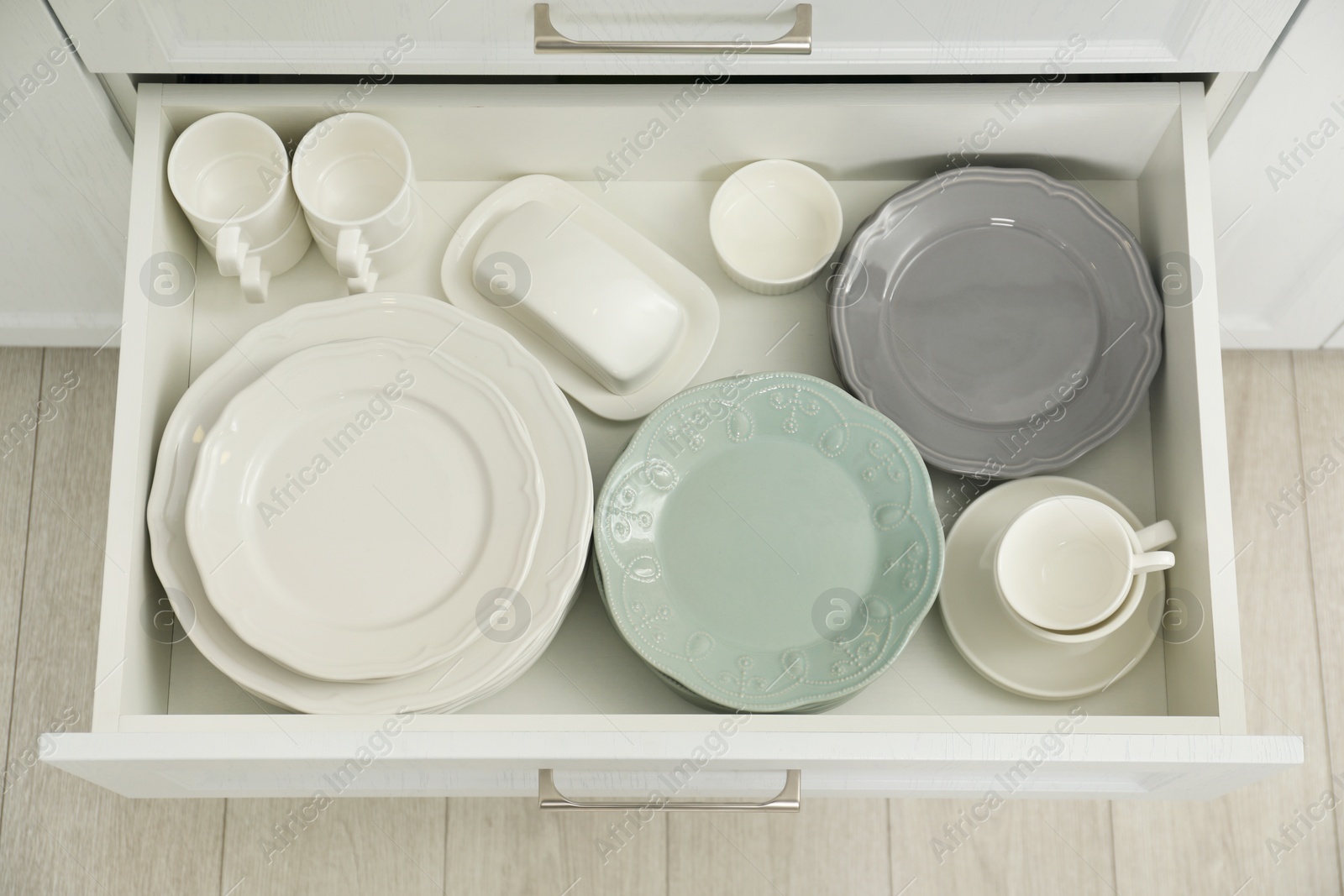 Photo of Clean plates, cups, butter dish and bowl in drawer indoors, top view