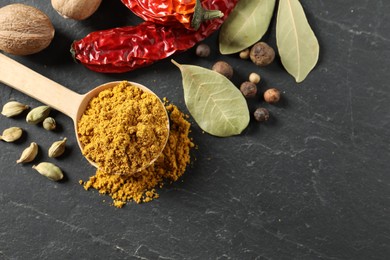 Photo of Spoon with dry curry powder and other spices on dark textured table, flat lay. Space for text