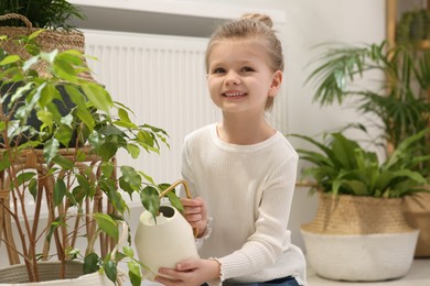 Photo of Cute little girl holding watering can near beautiful green plant at home. House decor