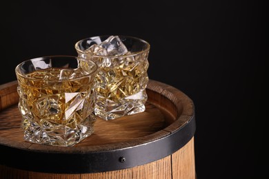 Photo of Whiskey in glasses on wooden barrel against dark background