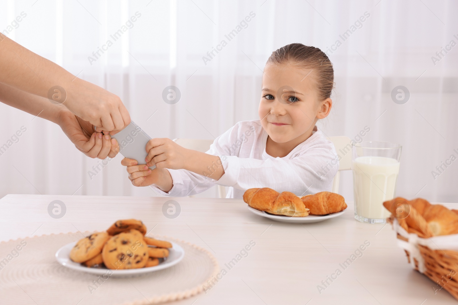 Photo of Woman taking away smartphone from her daughter at table indoors, closeup. Internet addiction