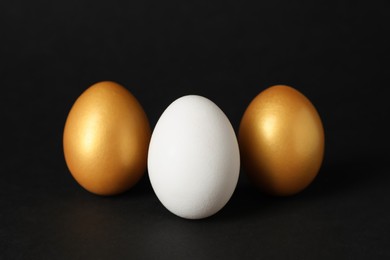 Golden and ordinary chicken eggs on black background