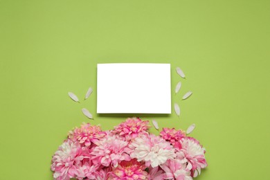 Beautiful chrysanthemums and blank card on light green background, flat lay. Space for text