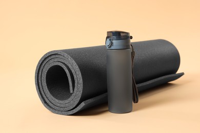 Photo of Grey yoga mat and bottle of water on beige background