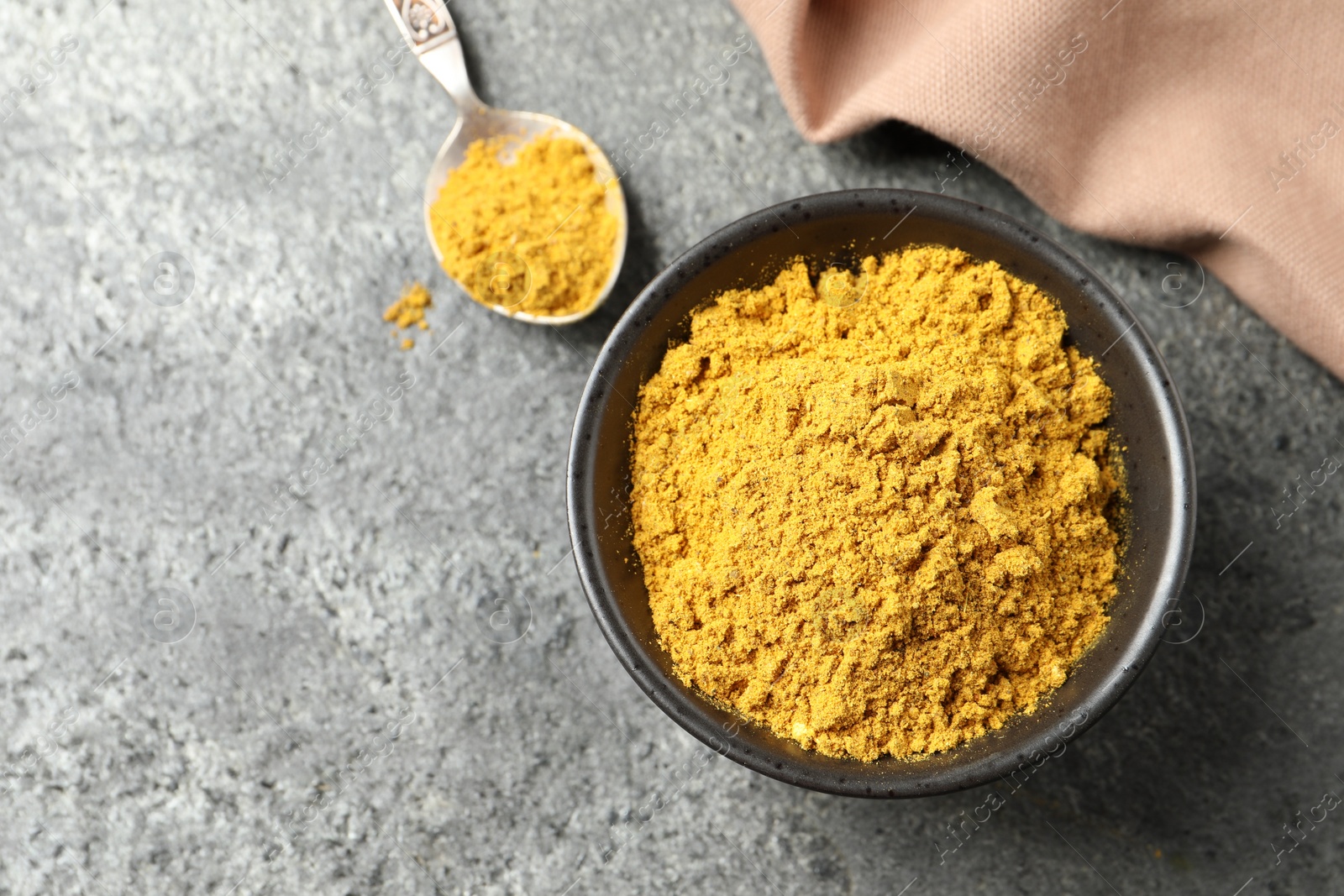 Photo of Dry curry powder in bowl and spoon on dark textured table, top view. Space for text