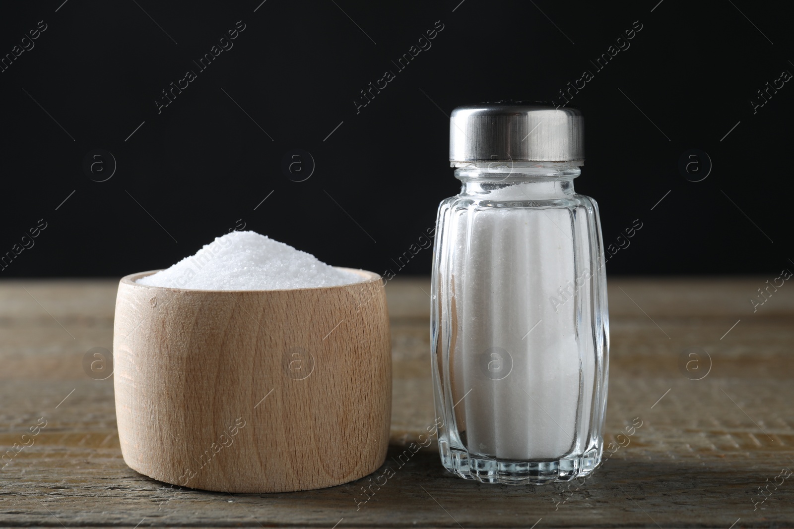 Photo of Organic salt in bowl and glass shaker on wooden table, closeup