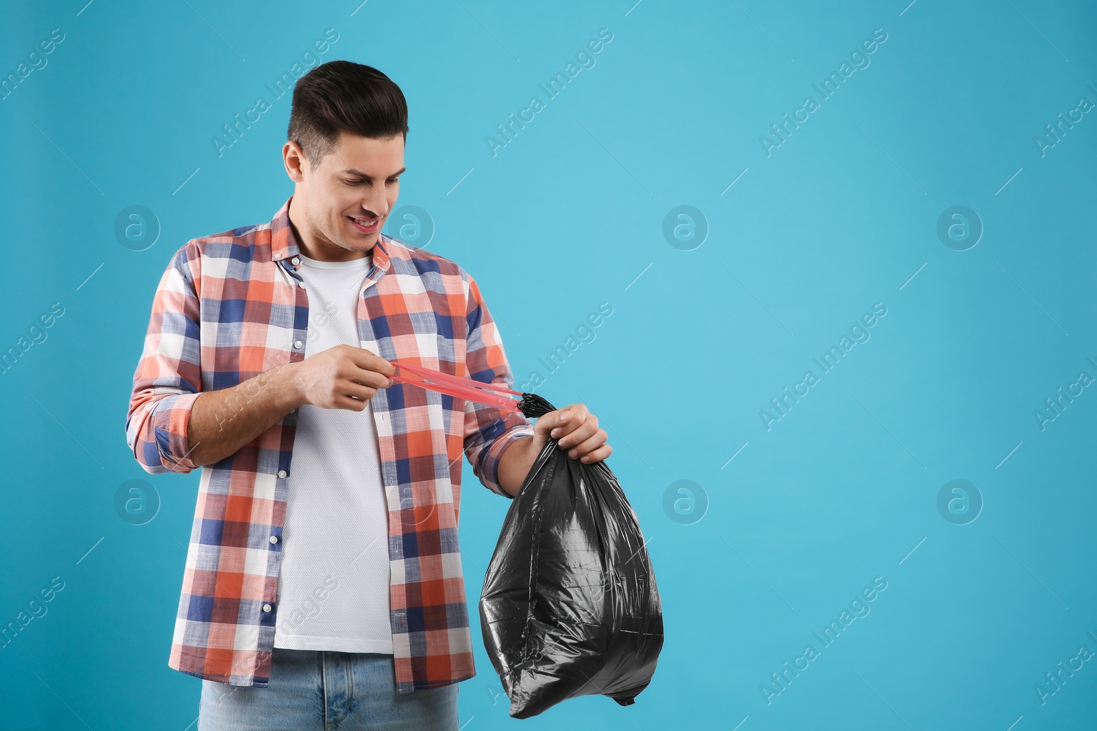 Photo of Man holding full garbage bag on light blue background. Space for text