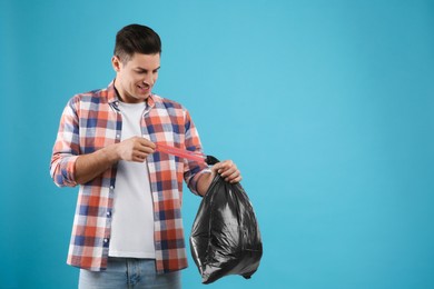 Photo of Man holding full garbage bag on light blue background. Space for text