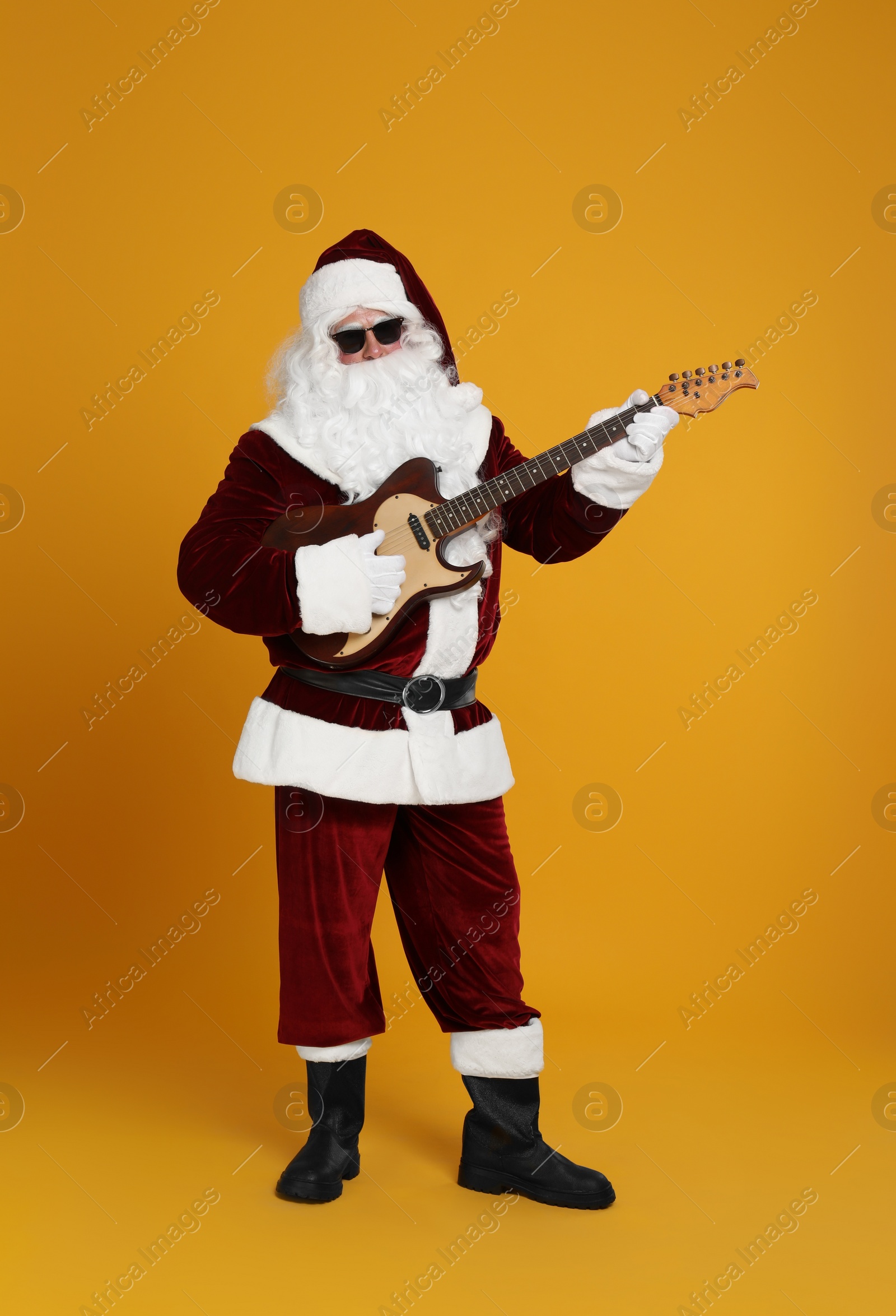 Photo of Santa Claus playing electric guitar on yellow background. Christmas music