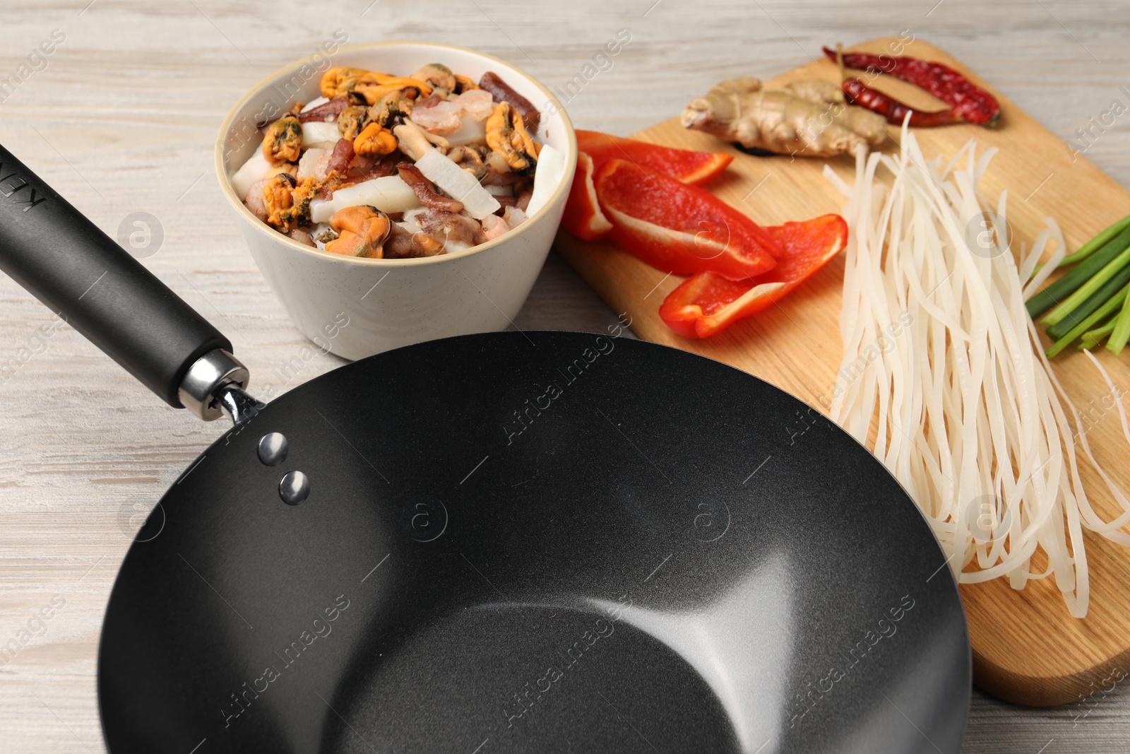 Photo of Black wok and products on light wooden table, closeup