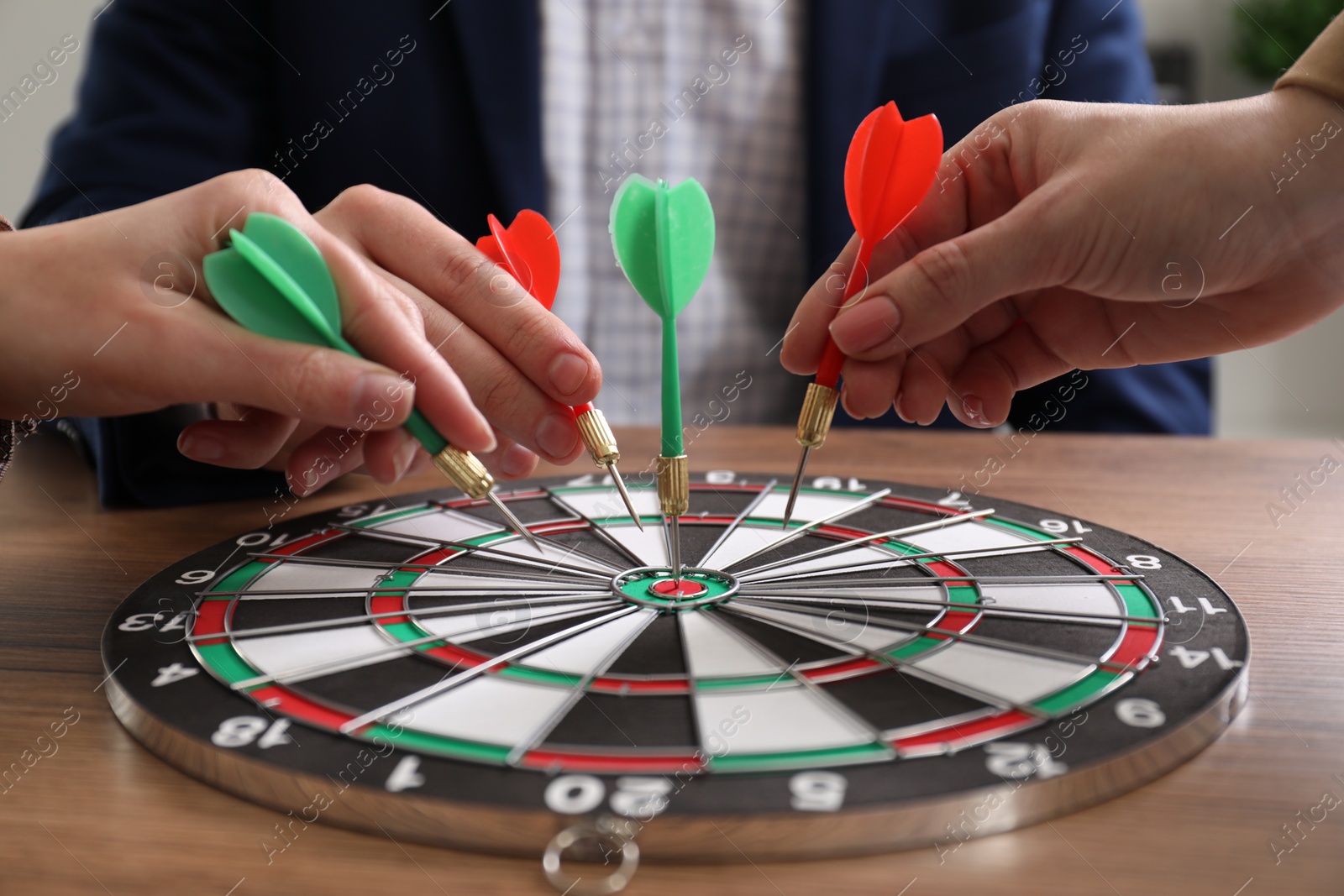 Photo of Business targeting concept. People with darts aiming at dartboard at table, closeup