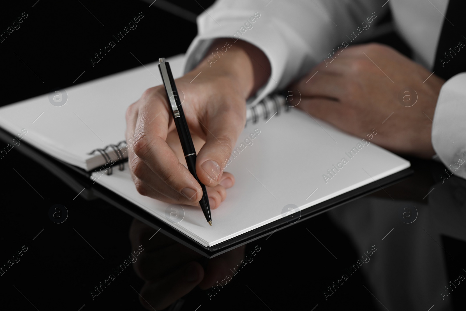 Photo of Man writing in notebook at black table, closeup