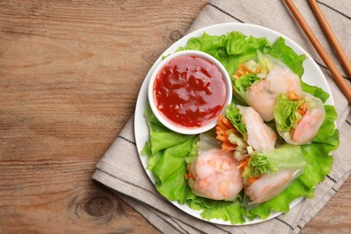 Photo of Tasty spring rolls served with lettuce and sauce on wooden table, top view. Space for text