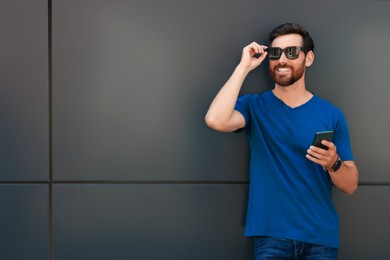 Happy man with smartphone near grey wall. Space for text