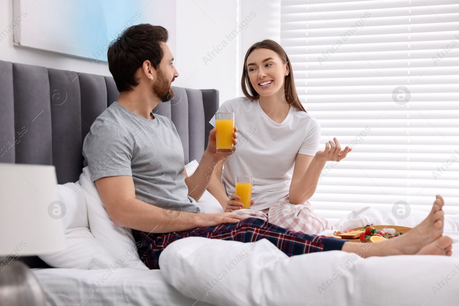 Photo of Happy couple having breakfast and talking on bed at home