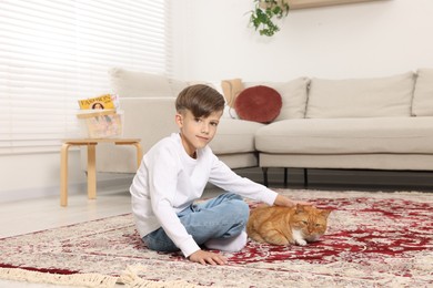 Little boy petting cute ginger cat on carpet at home