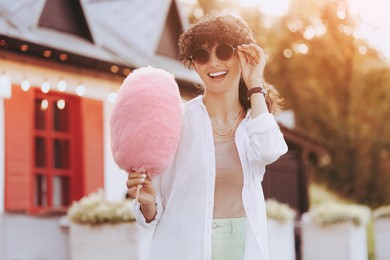 Image of Portrait of smiling woman with cotton candy outdoors on sunny day