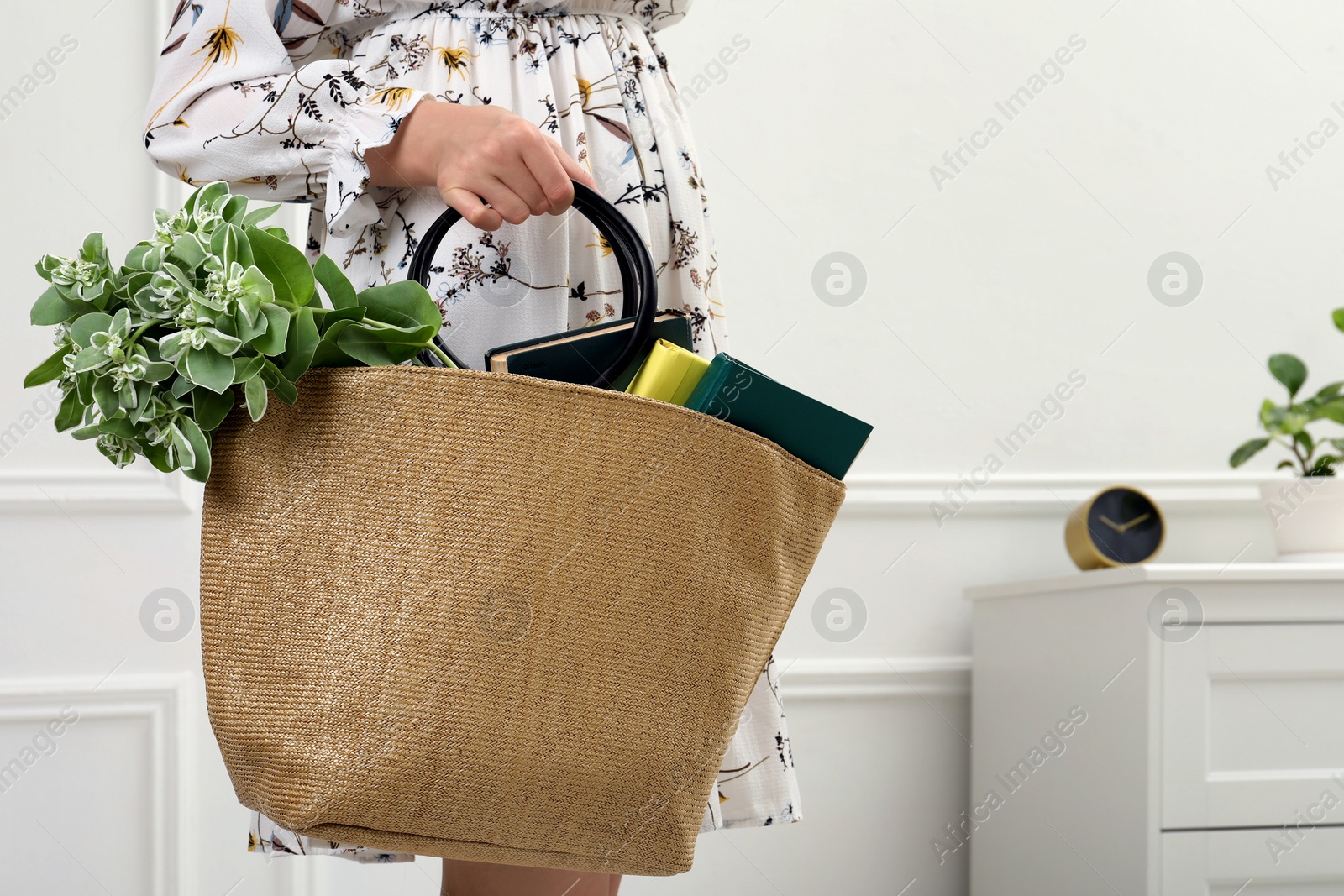 Photo of Woman holding beach bag with beautiful plant and books indoors, closeup