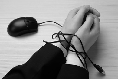 Image of Closeup view of woman with her hands tangled in cable of computer mouse at wooden table, black and white effect. Internet addiction