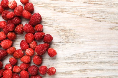 Many fresh wild strawberries on white wooden table, flat lay. Space for text