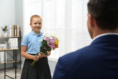 Schoolgirl with bouquet congratulating her pedagogue in classroom. Teacher's day