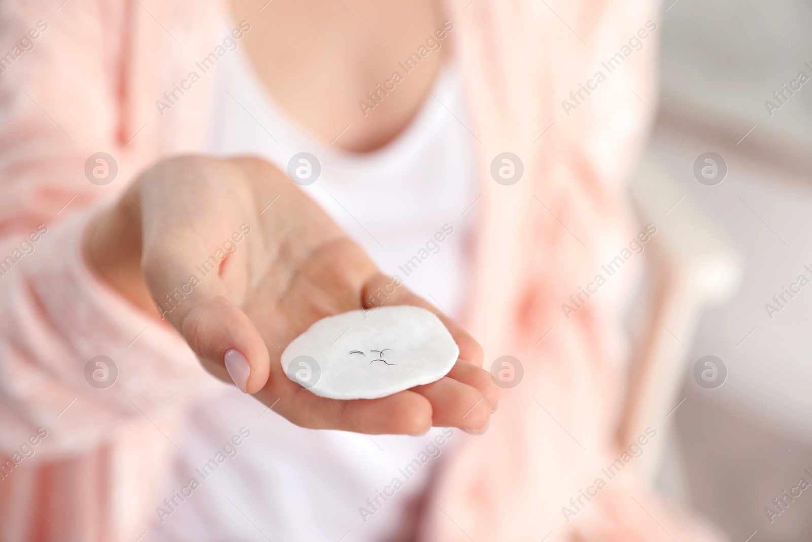 Photo of Young woman holding cotton pad with fallen eyelashes indoors