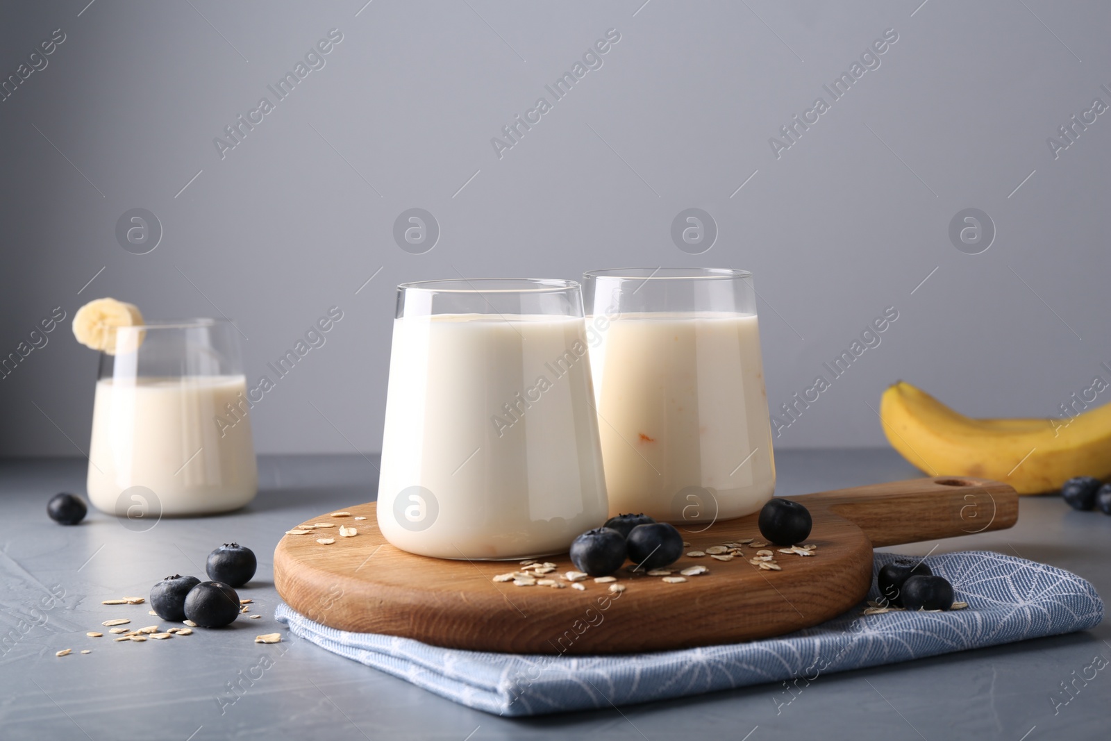 Photo of Tasty yogurt in glasses, oats and blueberries on grey table