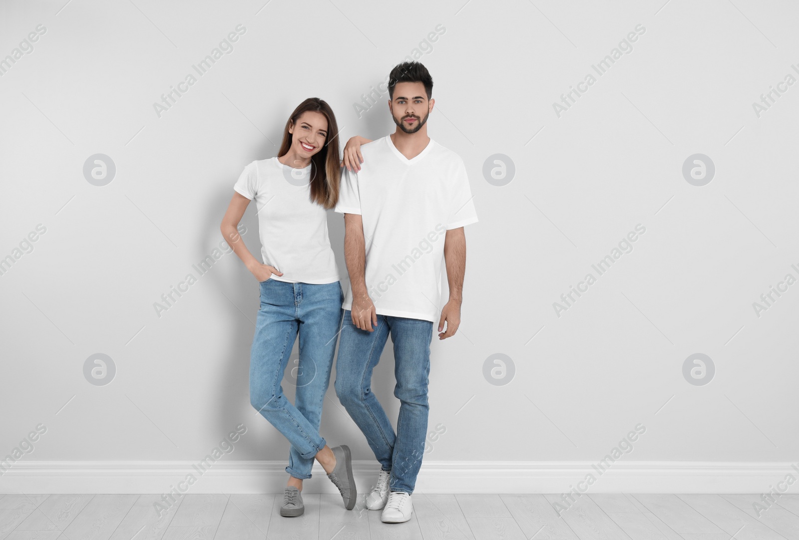 Photo of Young couple in stylish jeans near light wall