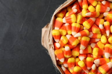 Photo of Paper bag with tasty candy corns on dark table, top view. Space for text