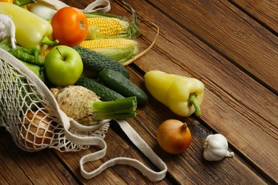 Photo of Different fresh vegetables in net bag on wooden table, closeup. Farmer harvesting